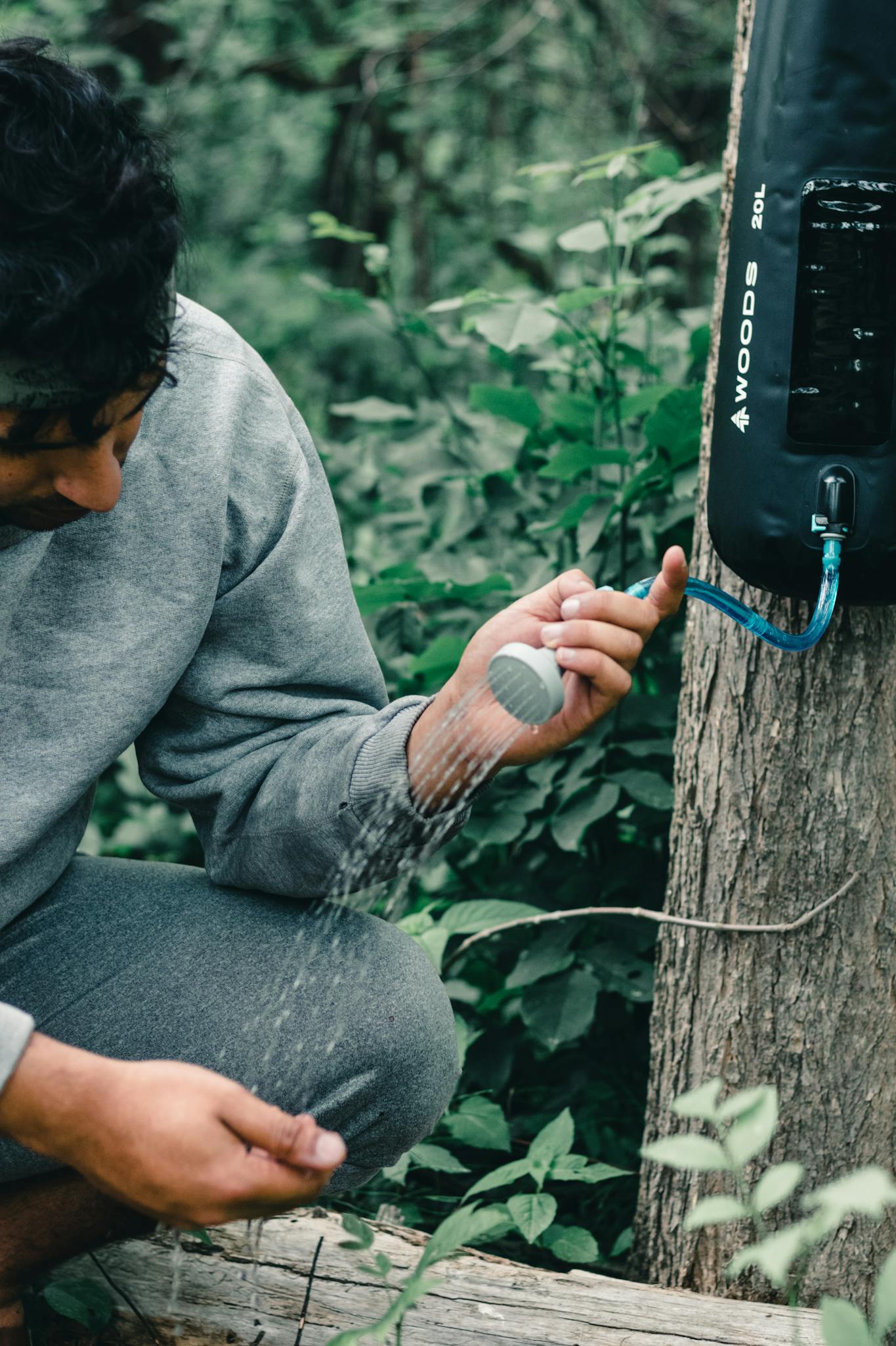 A person using an outdoor camping shower surrounded by lush Canadian forest.