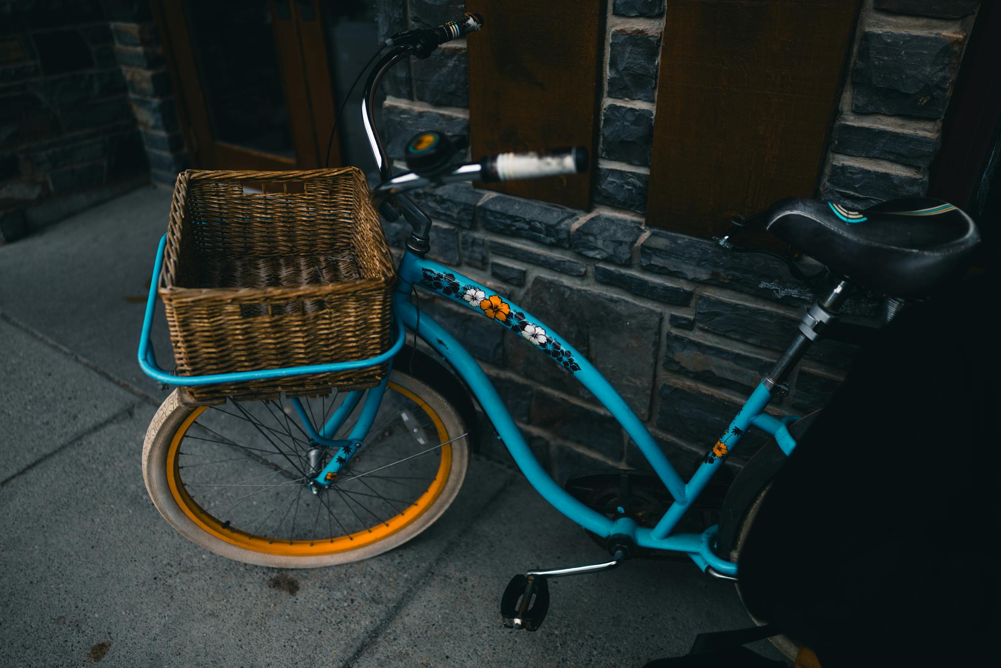 A stylish blue bicycle with a wicker basket against a stone wall in Banff, Alberta.